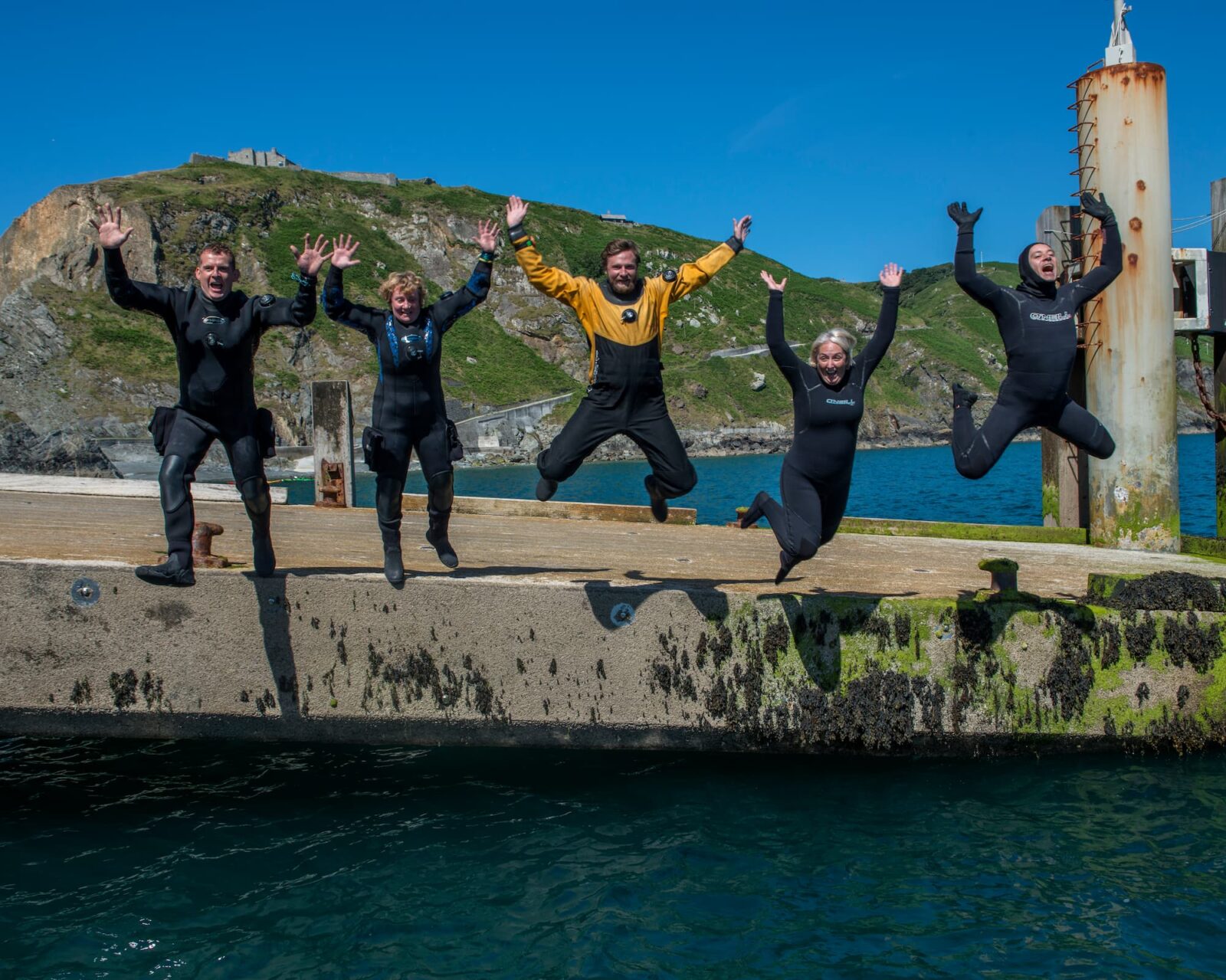 Jane Morgan Lundy Group-Topside-UK-five divers jumping from harbour into water